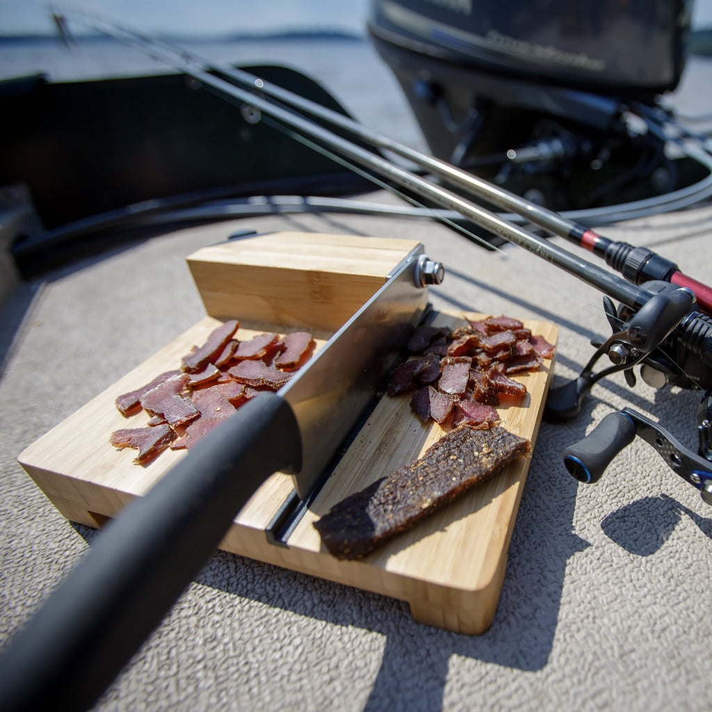 Wooden cutting board with a sliced biltong slab on a boat deck.