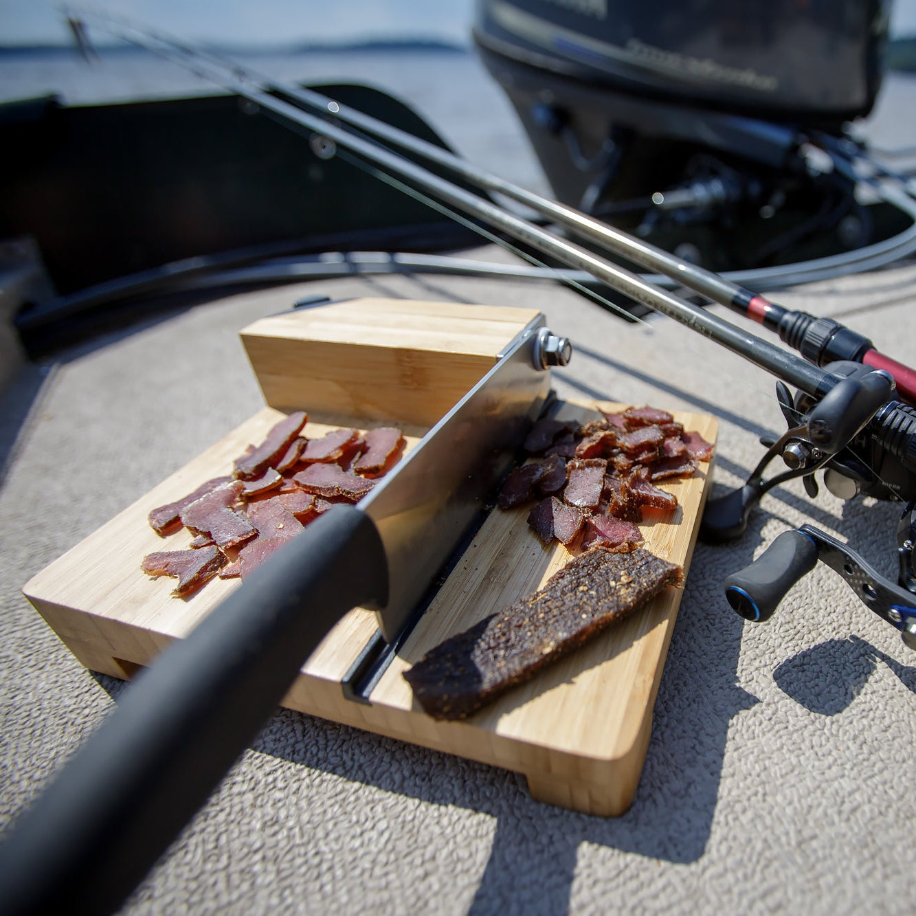 Wooden cutting board with a sliced biltong slab on a boat deck.