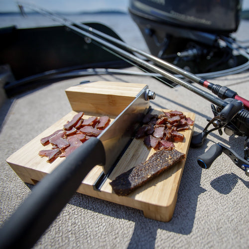 Wooden cutting board with a sliced biltong slab on a boat deck.