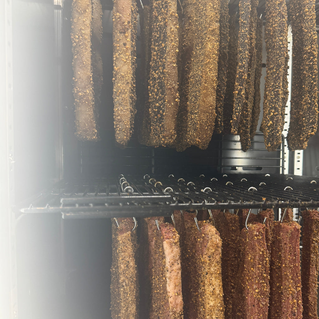 A row of wet biltong slabs hanging on a rack air drying