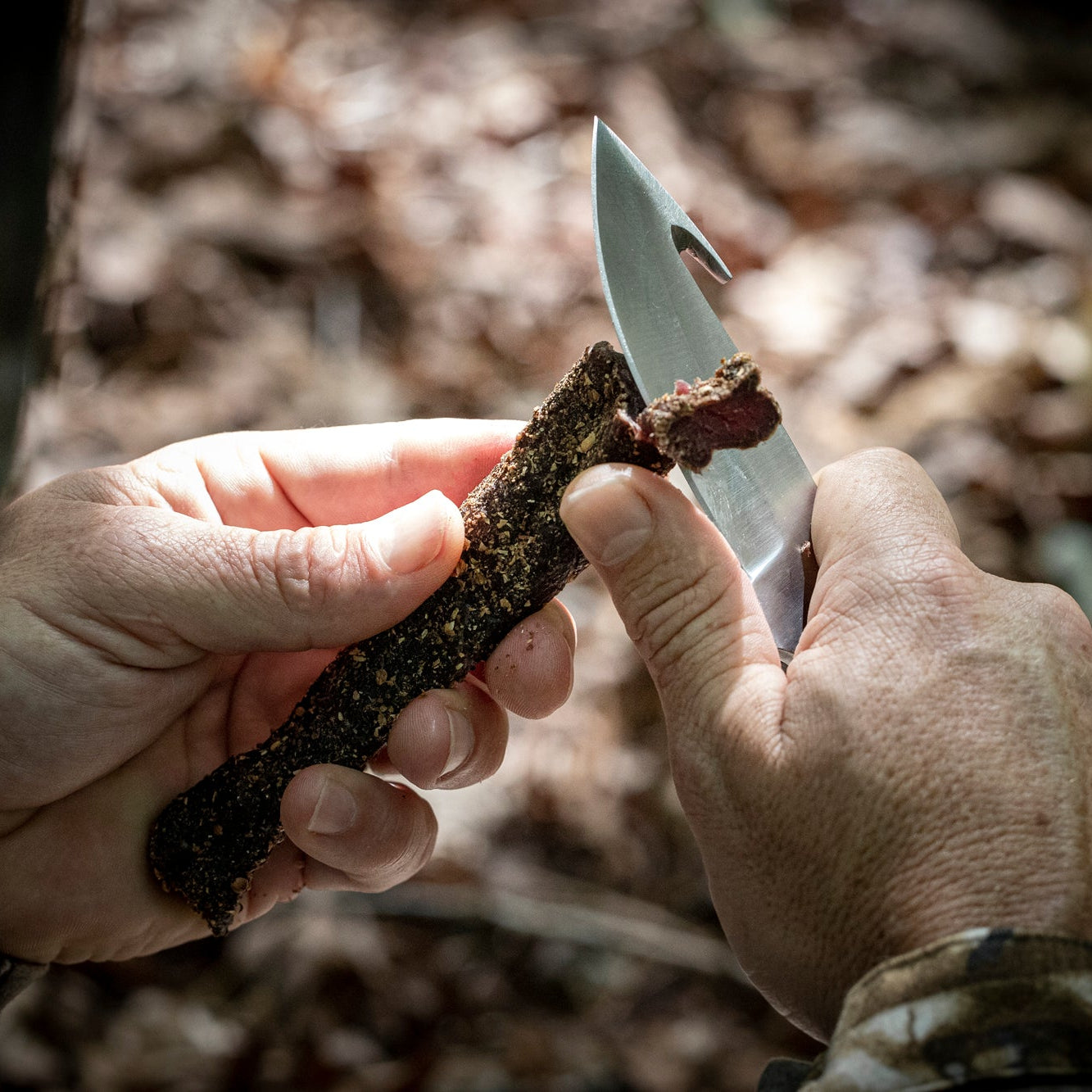 Person using a knife to cut a piece of biltong in a forest setting. A fidget spinner for hunters.