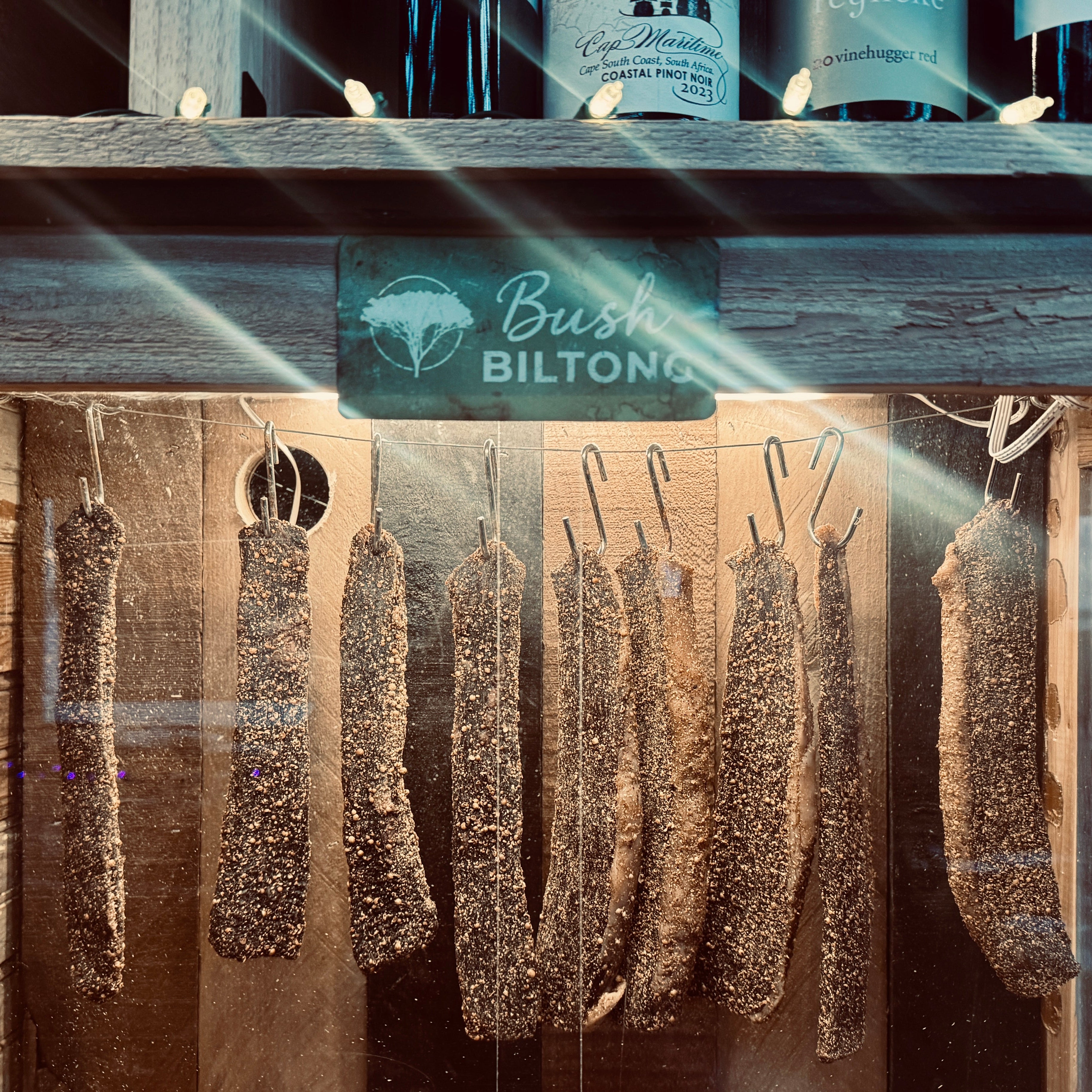 Biltong slabs hanging in a wooden biltong box with 'Bush Biltong' branding.