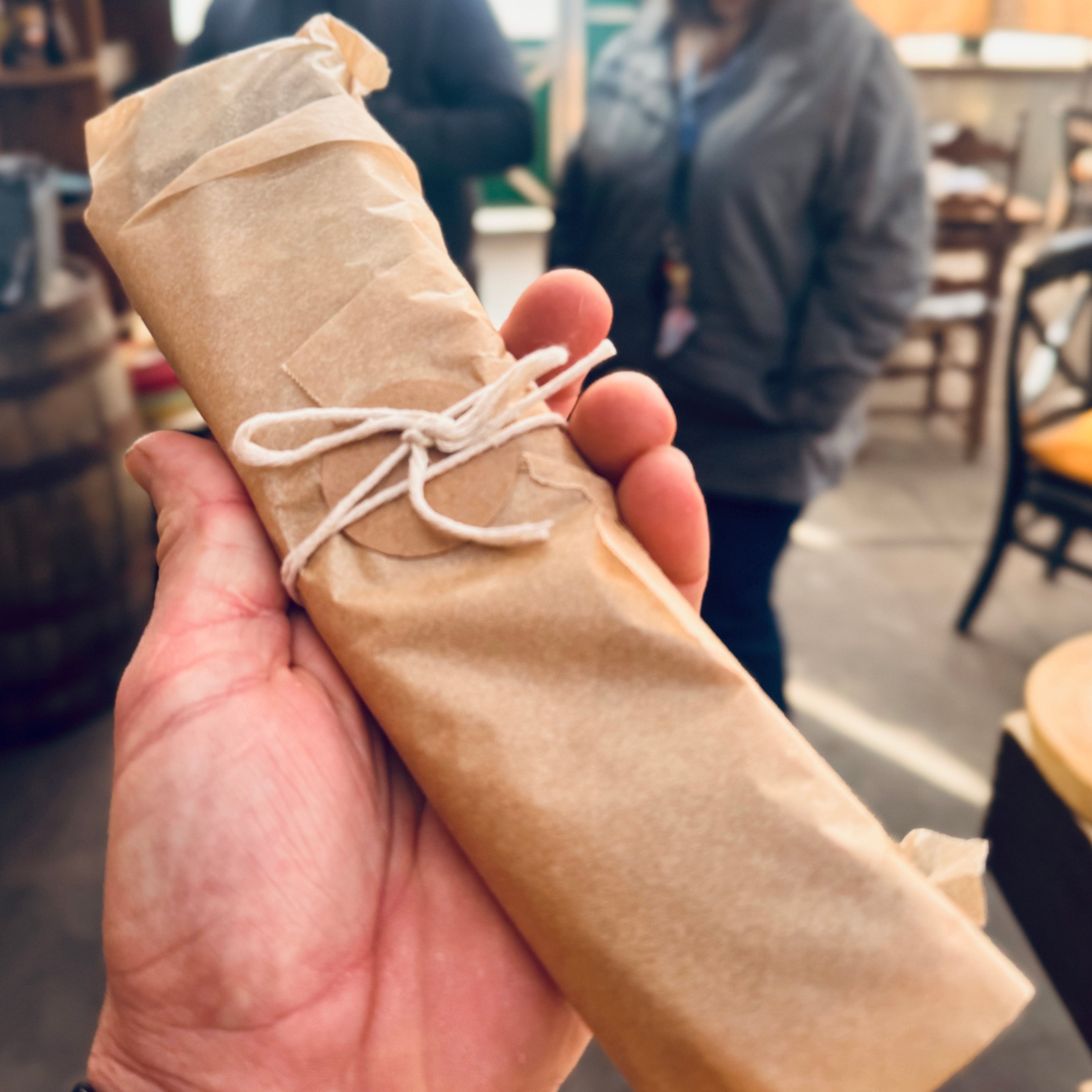 A person holding a whole slab of traditional South African biltong, wrapped in brown paper, at the Bush Farmhouse restaurant in Black Mountain, NC